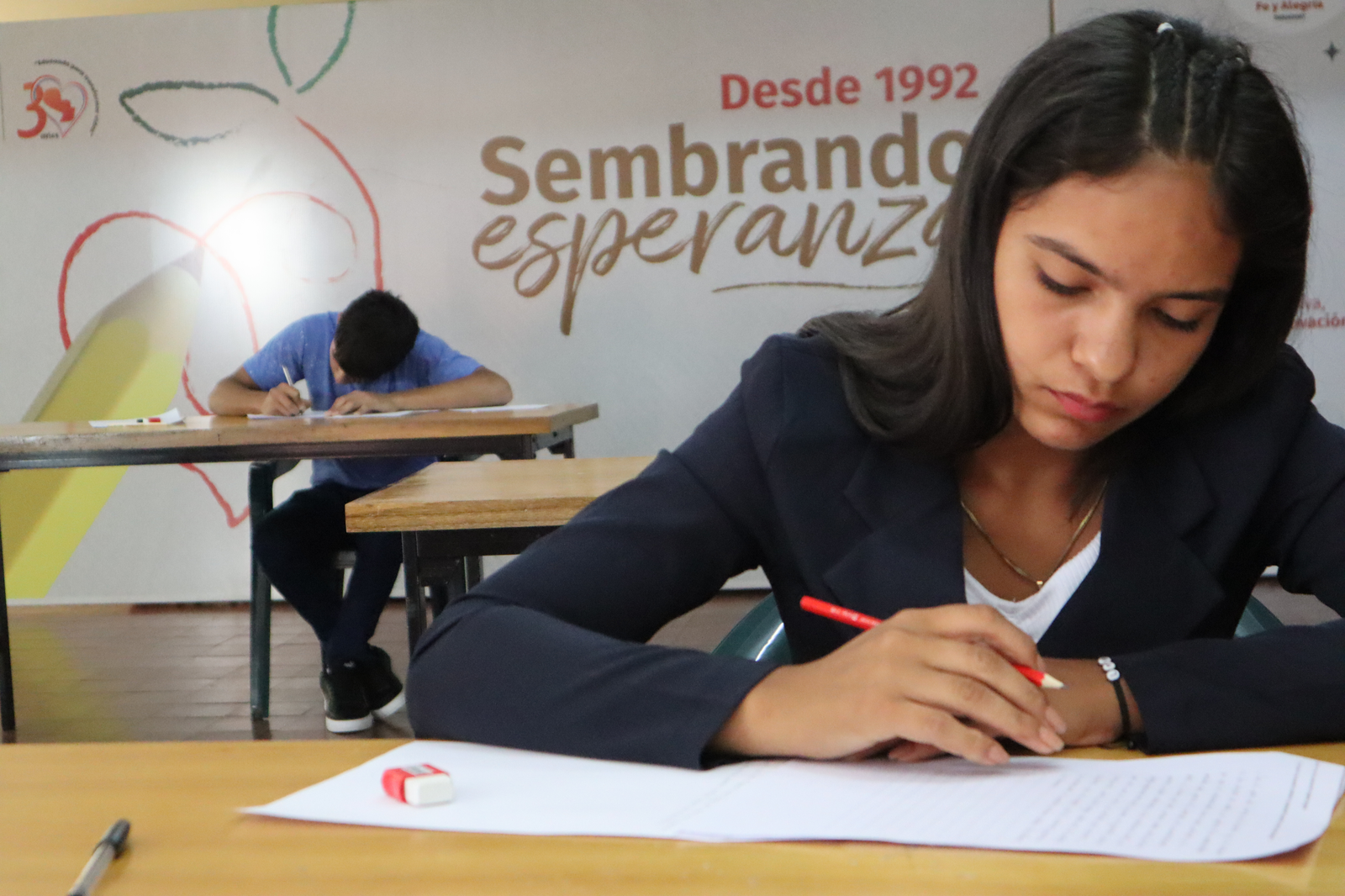 Estudiante de Fe y Alegría rindiendo examen, con el lema Sembrando esperanza al fondo