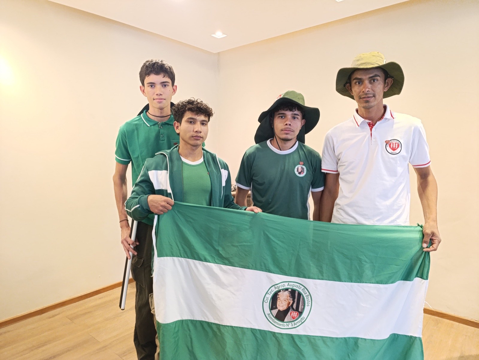 Los tres estudiantes y su docente acompañante sostienen la bandera del Colegio Técnico Agropecuario Augusto Roa Bastos