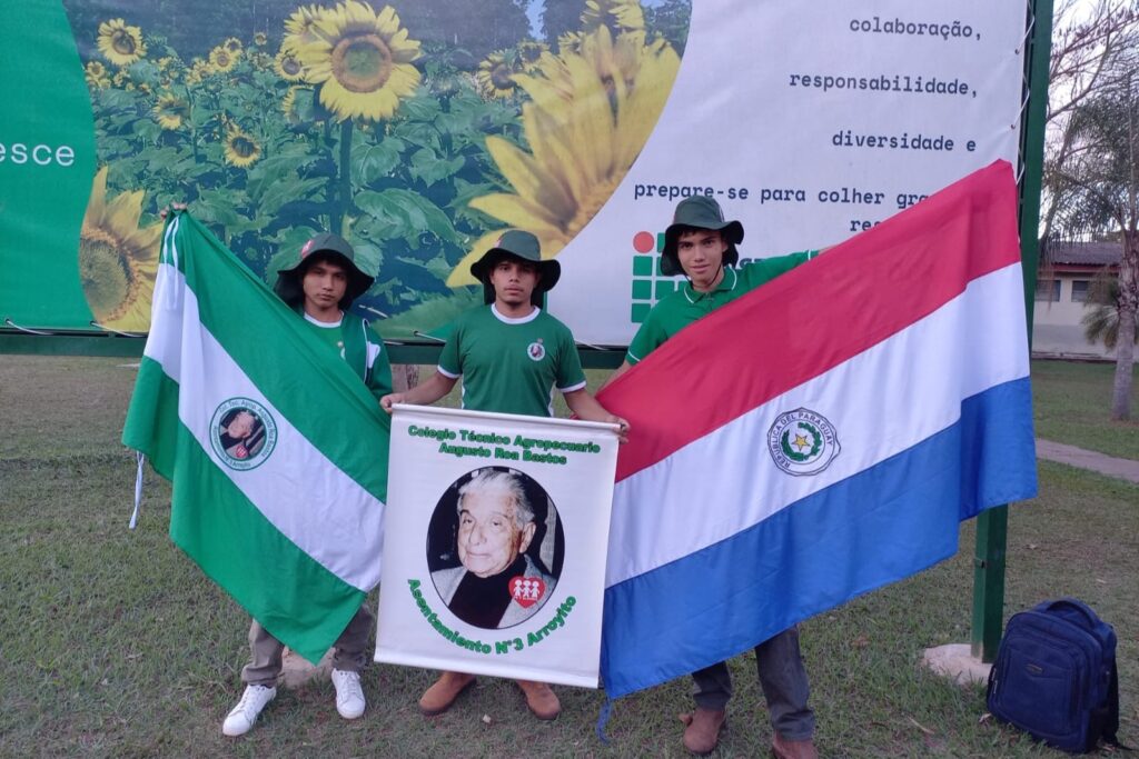 Tres estudiantes del Colegio Técnico Agropecuario Augusto Roa Bastos sostienen la bandera de Paraguay y el estandarte del colegio en la Olimpiada Brasileña Agropecuaria